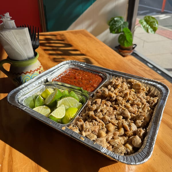 Aluminum tray with diced chicken, salsa, and lime wedges on a wooden table.
