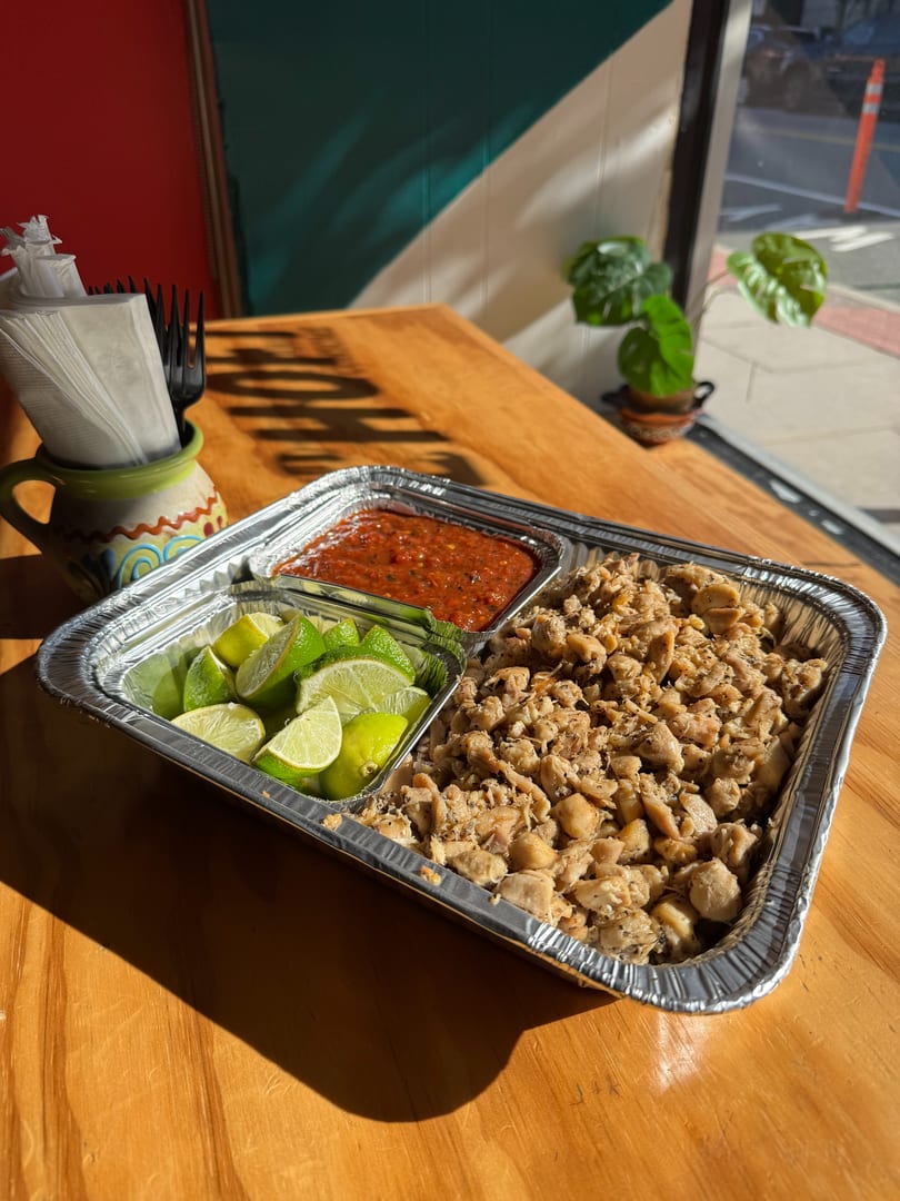 Aluminum tray with diced chicken, salsa, and lime wedges on a wooden table.