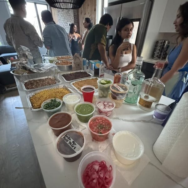 A buffet spread of Mexican food and condiments on a kitchen island with people mingling.